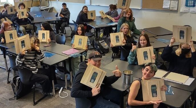 Students in classroom holding up calculator in wood cases.