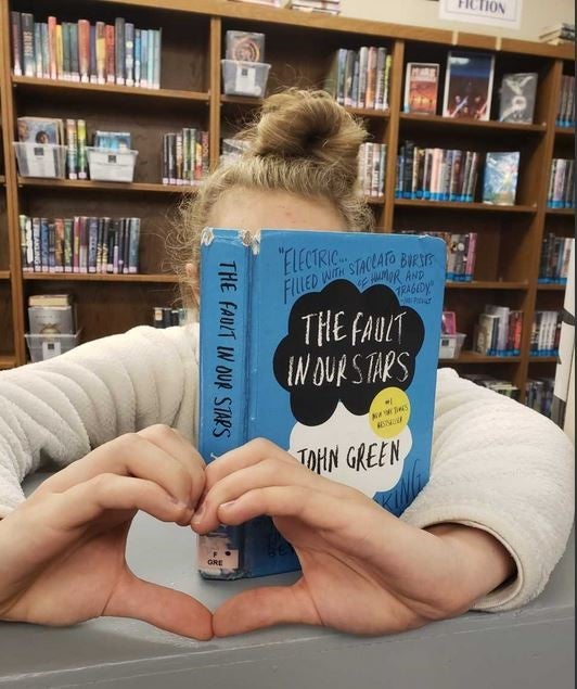TuesD with a book and making a heart with her hands